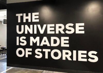 White cut vinyl lettering on a black wall reading "The universe is made of stories"